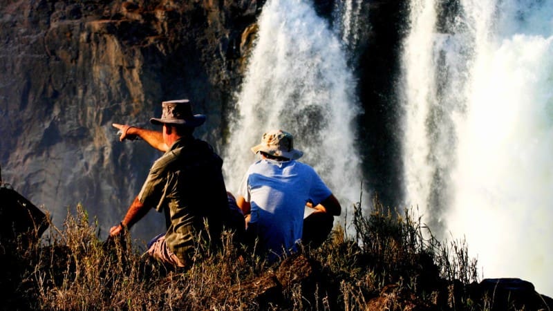 Trip To Victoria Falls Made Easy: Your Step-By-Step Guide 4 Travelers enjoying the view from a safe distance, a tip for staying cautious at Victoria Falls.