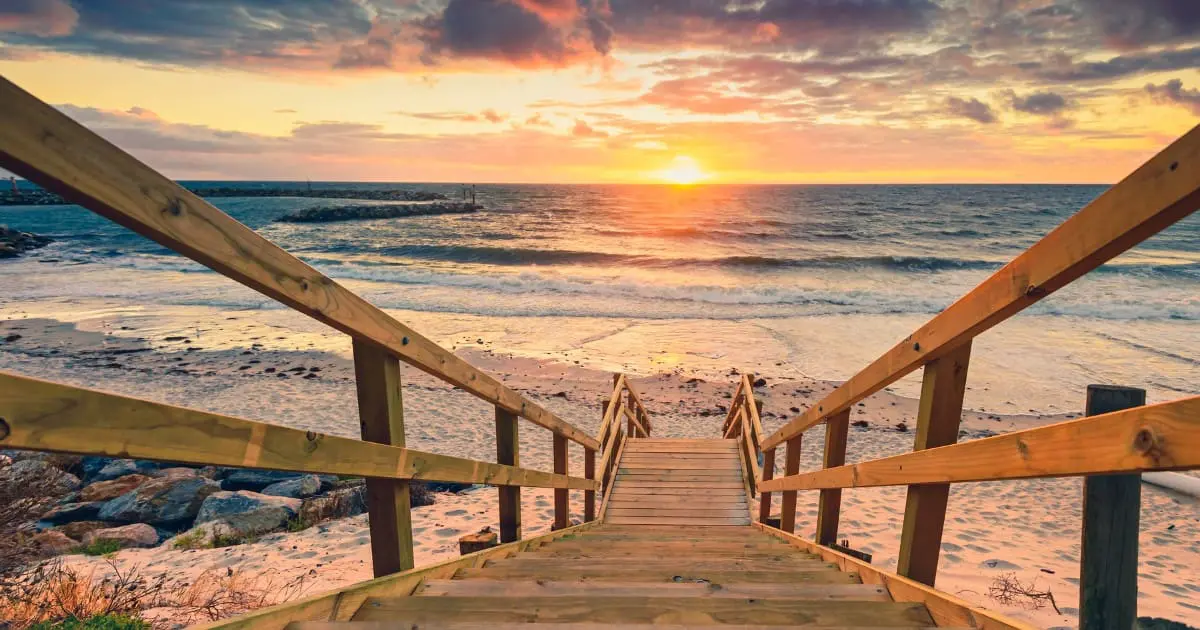 Free things to do in Adelaide - Wooden stairs leading to a tranquil beach during a stunning sunset, a perfect free activity.
