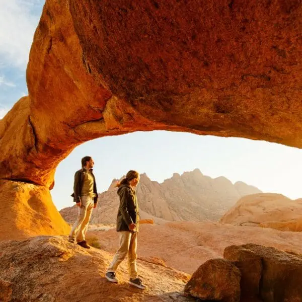 Two travelers under a natural rock arch, a highlight in any Namibia travel guide.