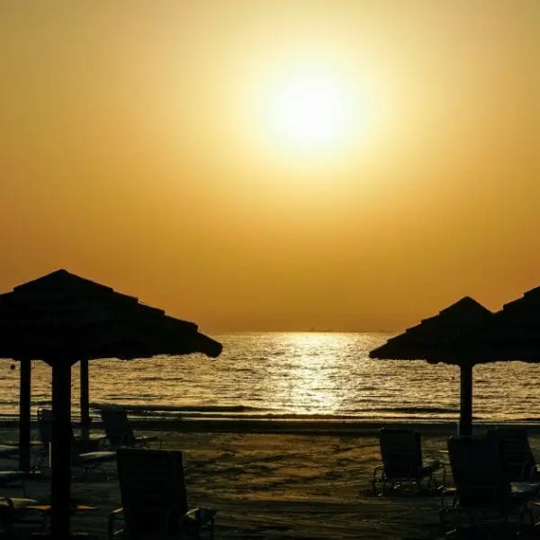 Places to visit in Ajman for free - Silhouettes of thatched umbrellas on a peaceful beach at sunset.