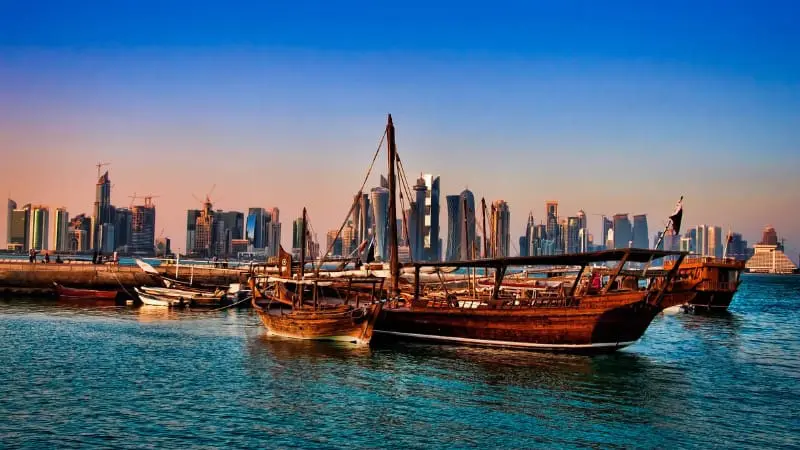Traditional wooden dhows docked in Ajman with the modern city in the background, free to see.