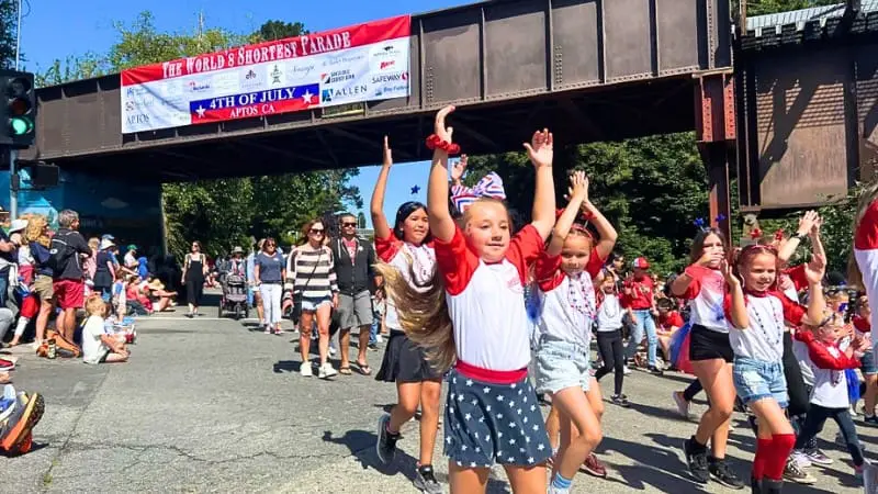 Kids joyfully march with arms raised under a 4th of July banner, ready for the 2024 festivities.