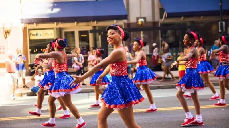 Cheerful girls in red, white and blue outfits march in a July 4th parade, an ideal 2024 event.