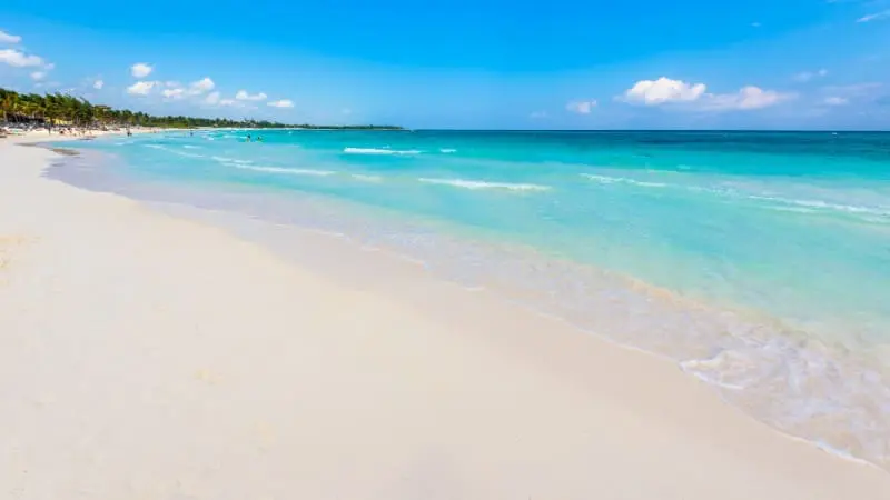 Playa Xpu-Ha features clear, calm waters, white sand, and a bright blue sky.