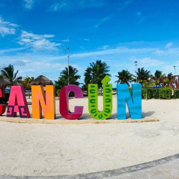 Best Beaches in Cancun - The colorful Cancun sign on a sandy beach with palm trees and blue skies.