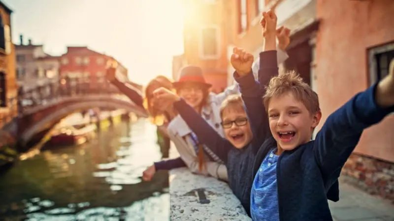 Excited kids cheer while touring Venice canals on a sunny Europe trip.