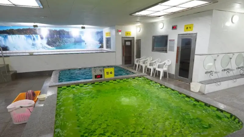 Korean sauna room with green mineral bath and waterfall mural.