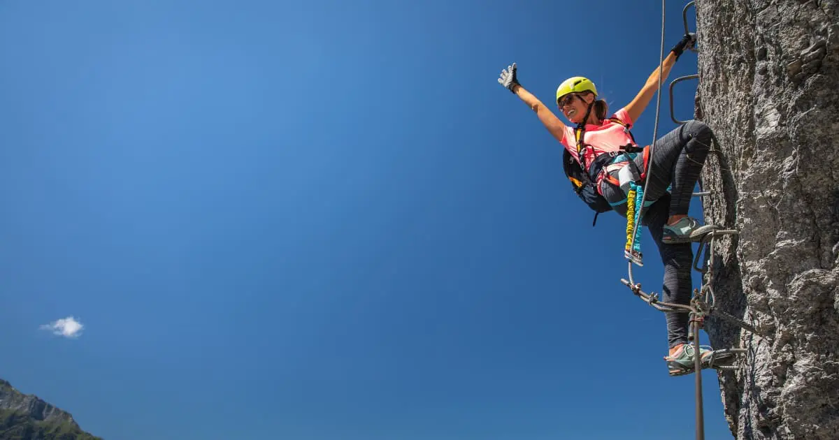 Climber celebrating reaching the top of Ouray Via Ferrata route with a clear blue sky.