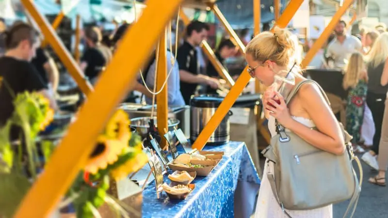 Woman sampling food at a bustling outdoor market in Banff during summer.