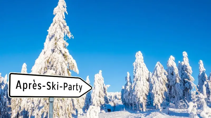 Snowy forest path with sign to après-ski party in Austrian winter landscape.