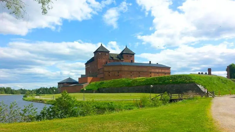 A big old castle with red bricks and green grass around it in Hämeenlinna.