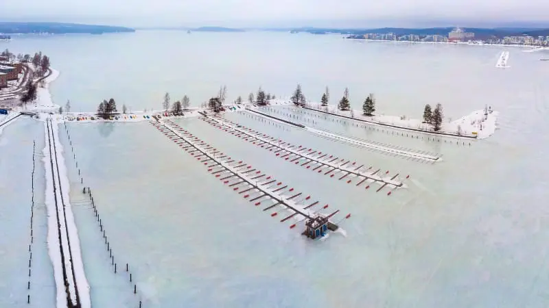 Boats docked in a frozen lake with a snowy city in the background in Lahti.