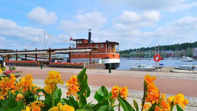 A boat docked by the water with bright flowers in front in Lappeenranta.