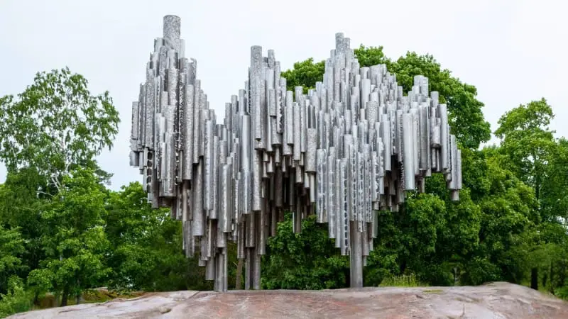 Abstract steel pipes of the Sibelius Monument rise above green trees.