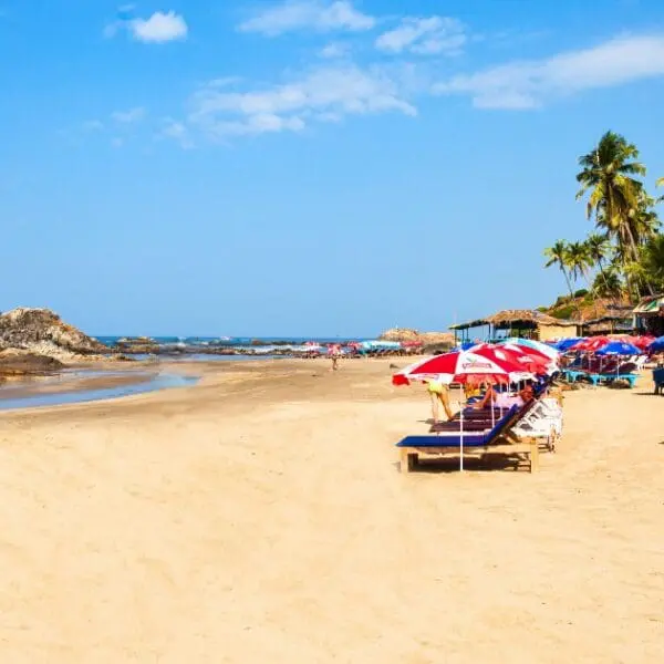 A serene view of Calangute Beach with clear skies, calm waters, and sunbeds.