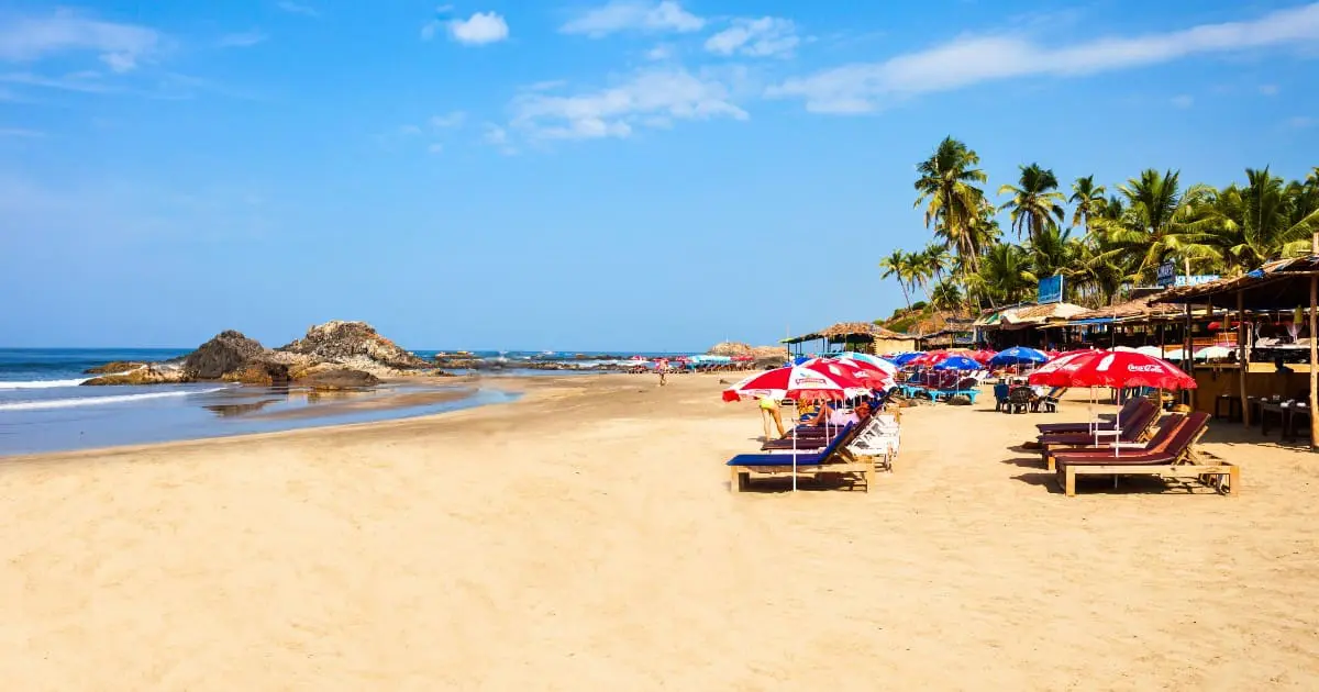 A serene view of Calangute Beach with clear skies, calm waters, and sunbeds.