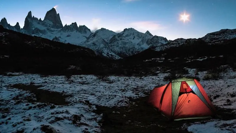 Your tent glows under starry skies near Mount Fitz Roys snowy peaks.