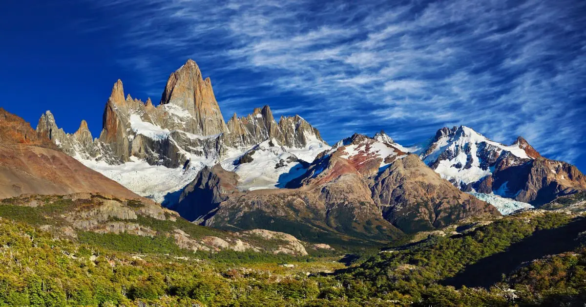 Mounts Fitz Roy has jagged peaks that rise high above green valleys on a clear day.