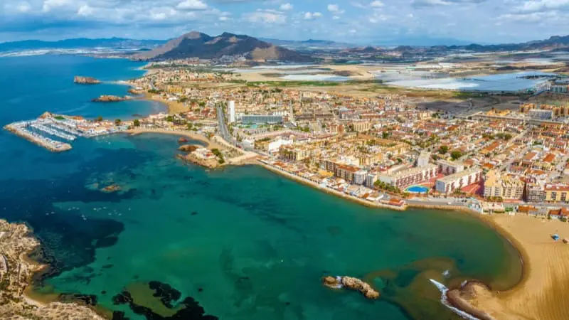 Aerial view of coastal town with clear blue waters and mountains.