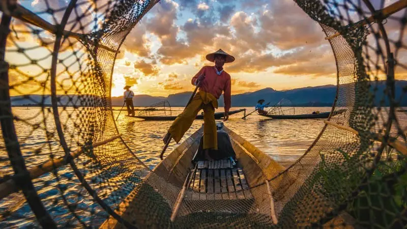 A fisherman rows with his leg on Inle Lake, using a unique traditional method.