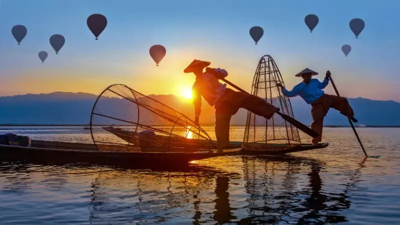 Fishermen use the famous leg-rowing technique on wooden boats at Inle Lake.