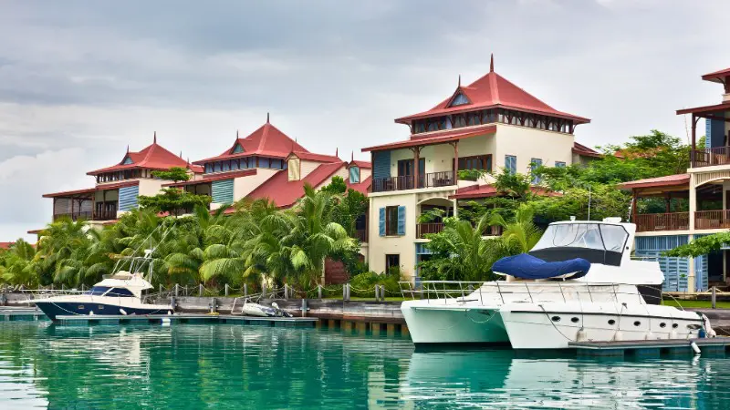 Luxury yachts docked by high-end resorts in a calm Seychelles bay.