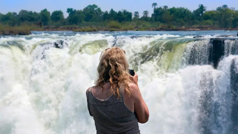 Tourist capturing the powerful waterfall on camera, highlighting the beauty of Victoria Falls.