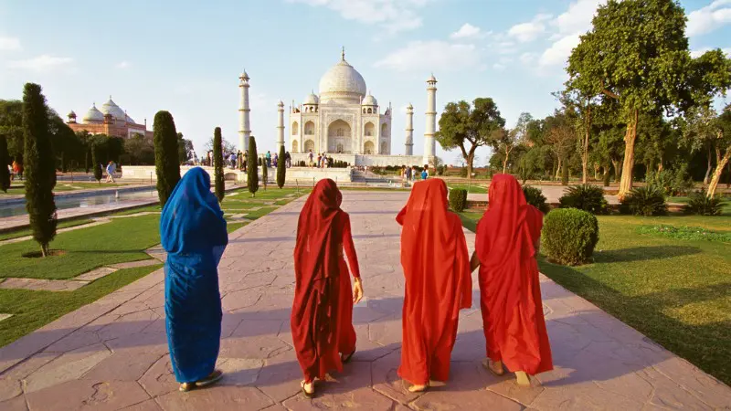 Tourists in colorful attire walk towards the stunning Taj Mahal.