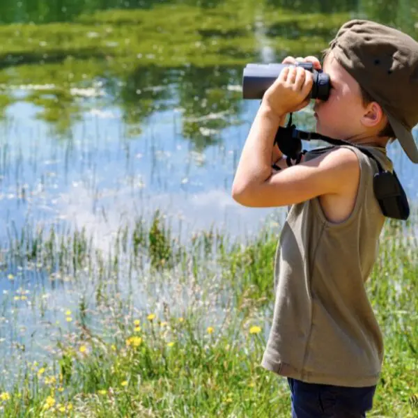 A child enjoys birdwatching by a serene lake in Trinidad and Tobago.