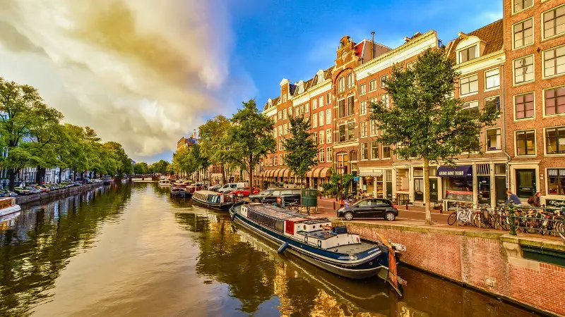Docked boats along the canals in Amsterdam with colorful historic buildings nearby.