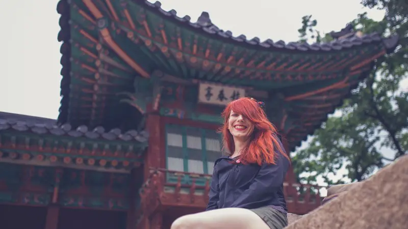 Smiling visitor at a traditional palace in Seoul with intricate architecture behind.