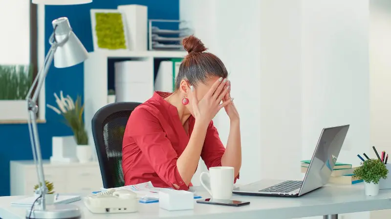 Woman in red shirt sits frustrated at desk learning complex hotel reward systems.