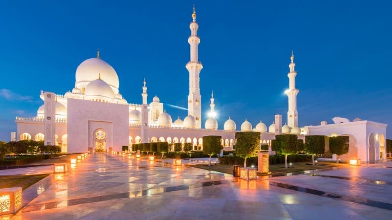 Free places to visit in Abu Dhabi - Sheikh Zayed Grand Mosque illuminated at dusk with white domes and minarets.