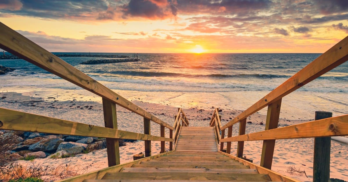 Free things to do in Adelaide - Wooden stairs leading to a tranquil beach during a stunning sunset, a perfect free activity.