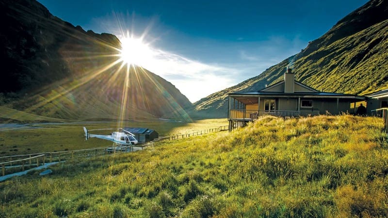 Sun rays illuminate a picturesque valley with a luxury New Zealand lodge, offering a tranquil escape from nature.