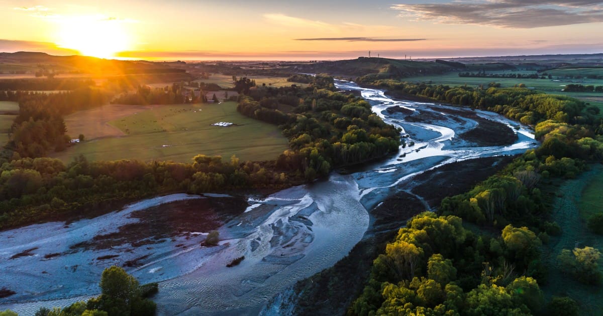 Luxury lodges to stay in New Zealand - Aerial view of a river winding through forests at sunset.