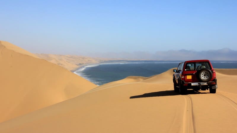 A 4x4 vehicle navigating the sand dunes of the Namib Desert, a must in any Namibia travel guide.
