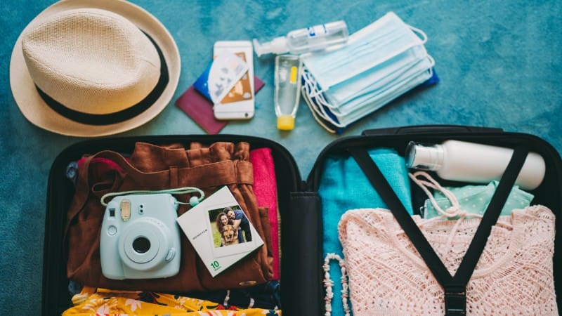 A neatly packed suitcase with travel essentials like a camera, hat, and face masks, perfect for a Namibia adventure.