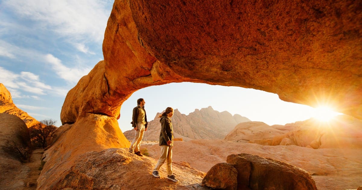 Two travelers under a natural rock arch, a highlight in any Namibia travel guide.