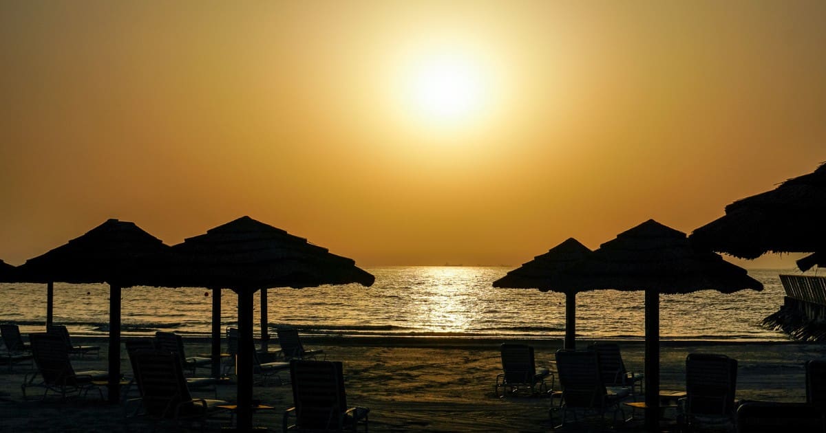 Places to visit in Ajman for free - Silhouettes of thatched umbrellas on a peaceful beach at sunset.