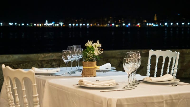 An elegantly set outdoor dining table with a view of Takapuna's twinkling lights at night, perfect for a romantic evening.