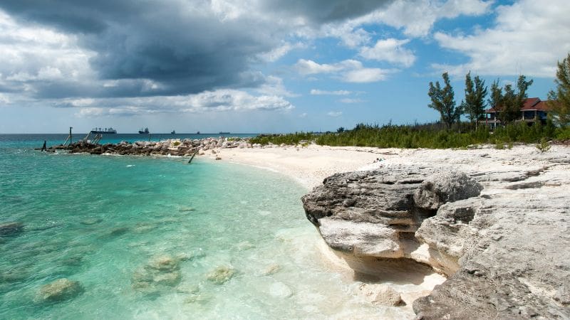 View of Grand Bahama Island featuring a sandy beach, turquoise waters, and a wooden pier under a cloudy sky.