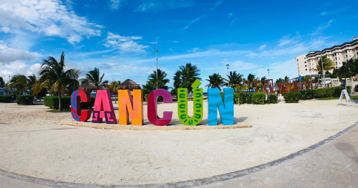 Best Beaches in Cancun - The colorful Cancun sign on a sandy beach with palm trees and blue skies.