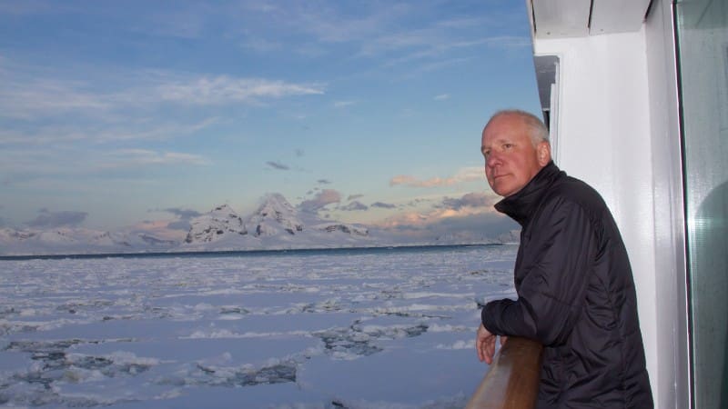 A tourist admires the icy landscape from a cruise ship deck.