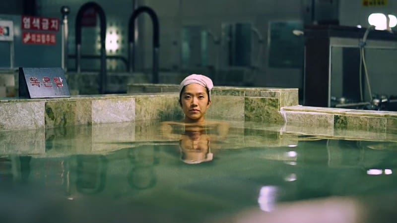 A woman soaks in the tranquil green waters of a Korean bathhouse, or jjimjilbang.