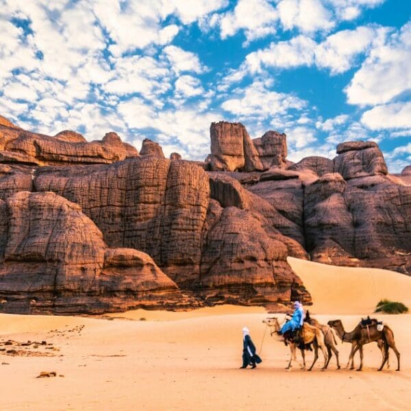 Places to visit in Algeria - Sahara desert with camels and unique rock formations.