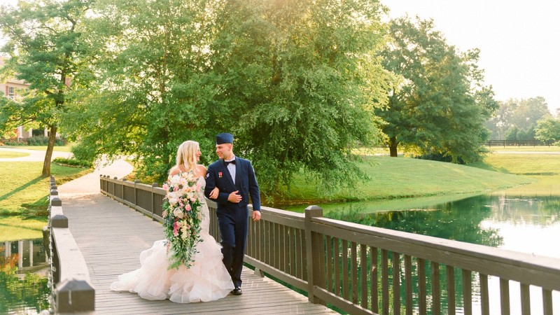 Wedding destinations in Alabama - Couple walks on bridge over pond in lush park.