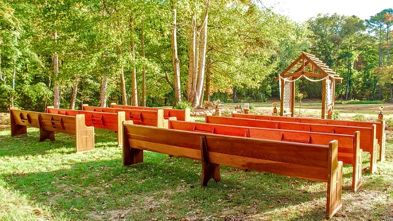 Rustic outdoor Alabama wedding venue with wooden benches and arbor in wooded area.
