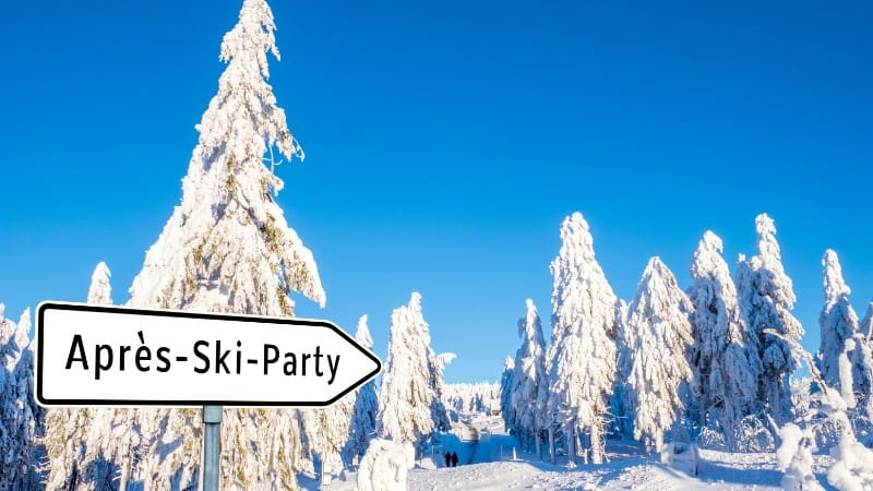 Snowy forest path with sign to après-ski party in Austrian winter landscape.