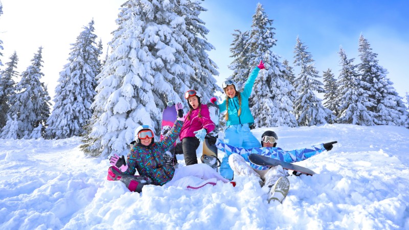 Cheerful group in Austria ski resort, frolicking in deep snow among snowy pines.